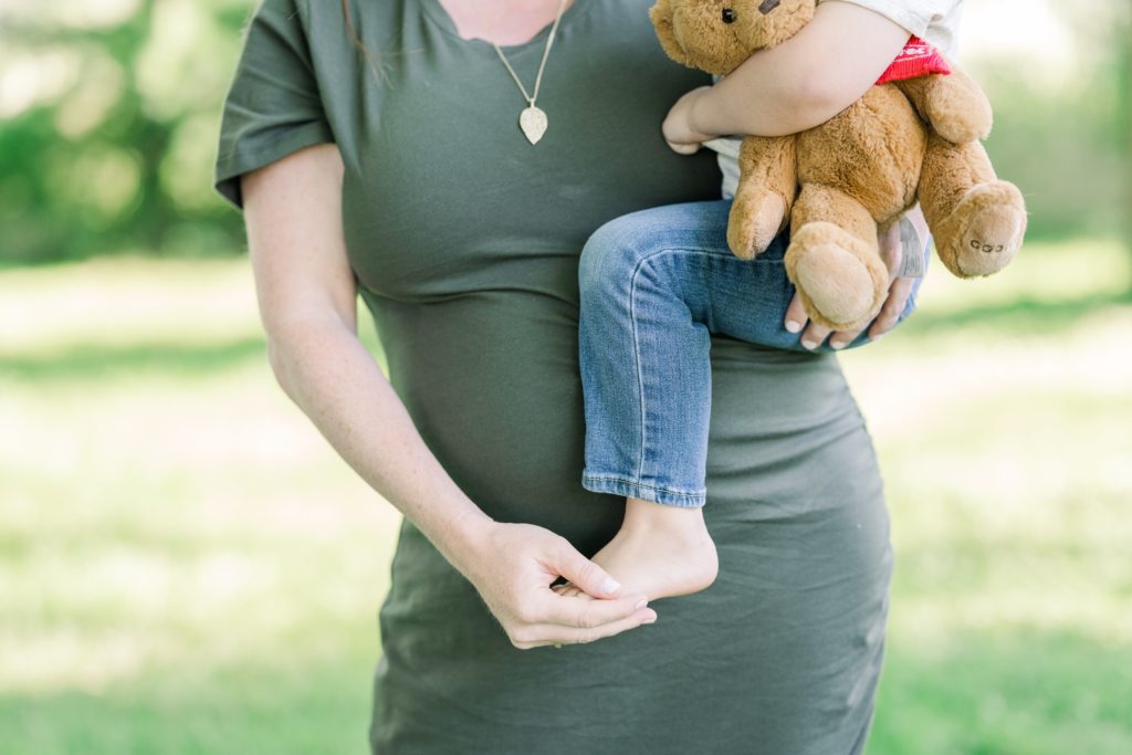 Barefoot toddler with teddy held by mom