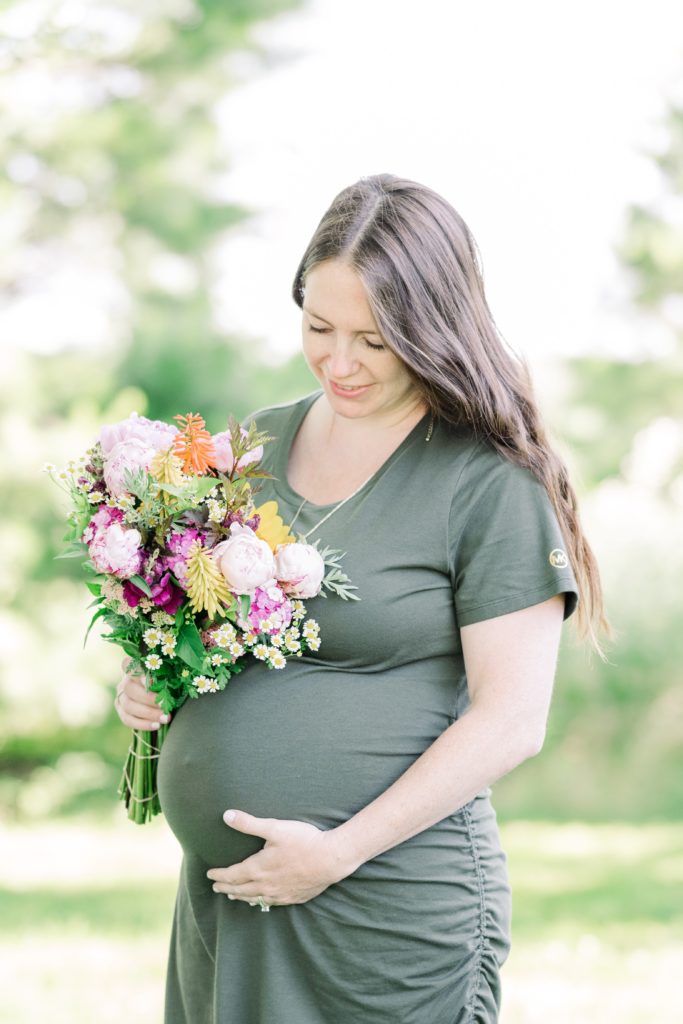 mom looking at baby bump at outdoor maternity session with fresh flowers