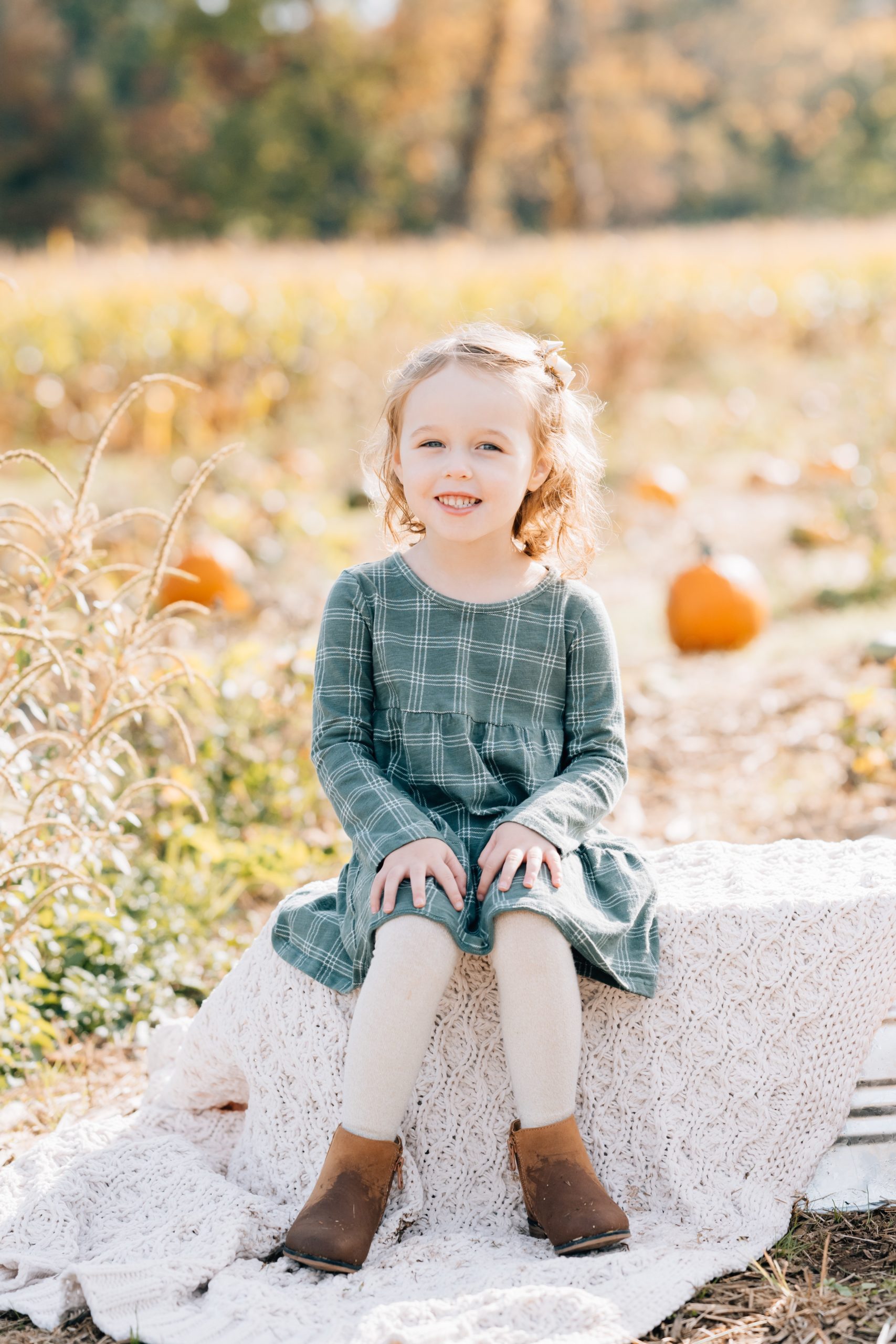 little girl poses on barrel seat with cream colored blanket in dusty teal dress at fall mini session with Maternity Photoshoot NJ Golden Heart Photography