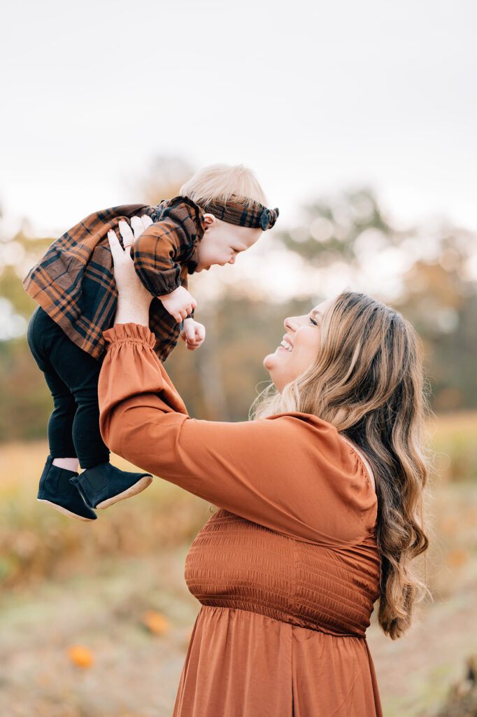 mom lifts up baby girl above head to make giggle at session with Golden Heart Photography