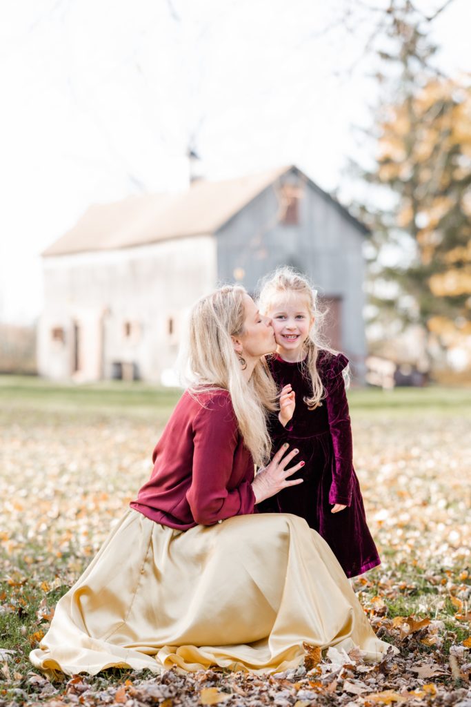 mom gives daughter a kiss in beautiful cranberry and gold outfits Holiday Mini Session | Five Birds Farm Ringoes | The Munz Family | Golden Heart Photography