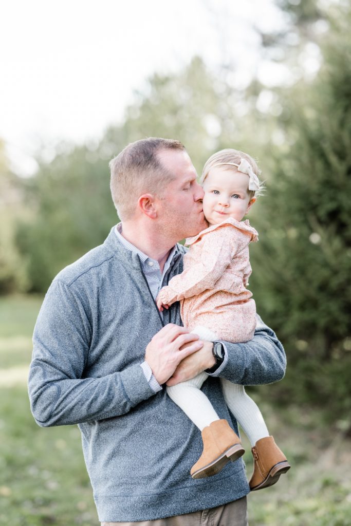 dad and daughter pose at Golden Heart Photography family session, dad kisses baby on cheek, pink floral romper dad in a complimentary blue