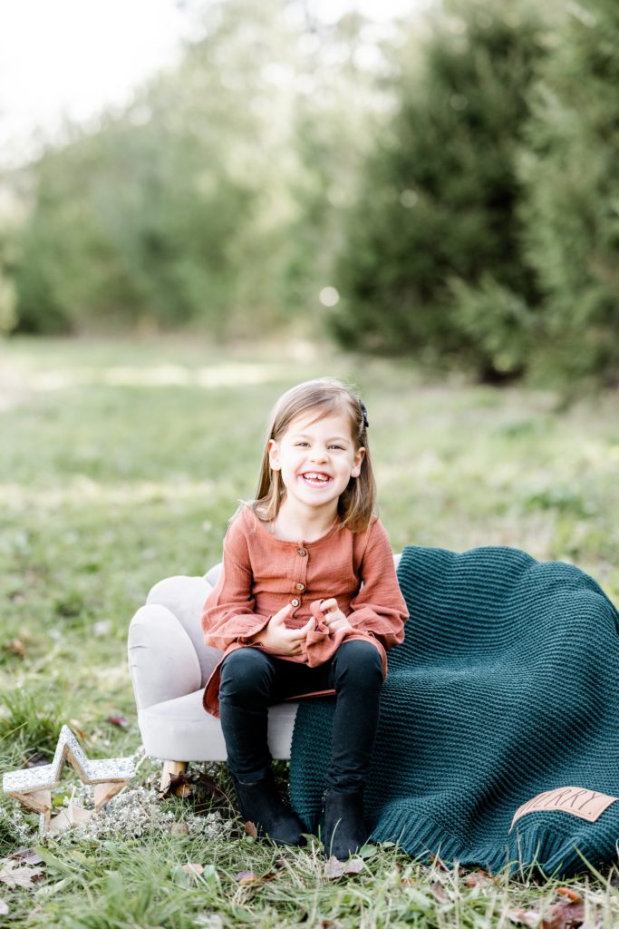 toddler girl poses on bench with excited smile in salmon colored muslin dress with black leggings with Golden Heart Photography