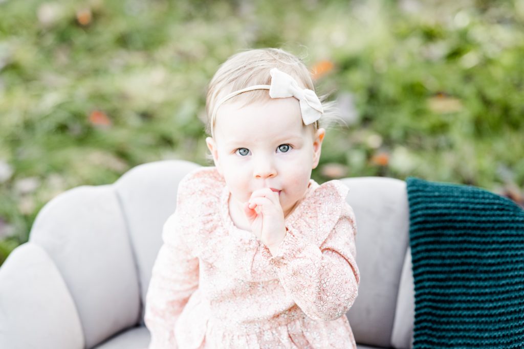 Holiday Mini Session | Hunterdon County Mini Sessions | The Furstenburg Family | Golden Heart Photography sweet baby sits on bench and looks at camera in soft pink outfit with matching bow