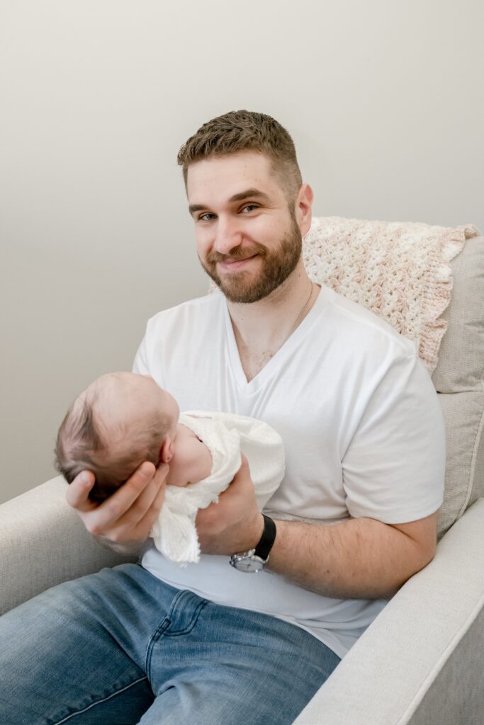 Dad poses holding baby daughter in nursery at session with Golden Heart Photography